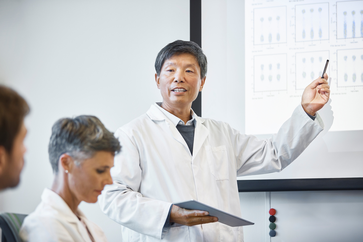 Mature professional giving presentation in meeting. Male scientist is discussing with colleagues. They are planning in board room at hospital.